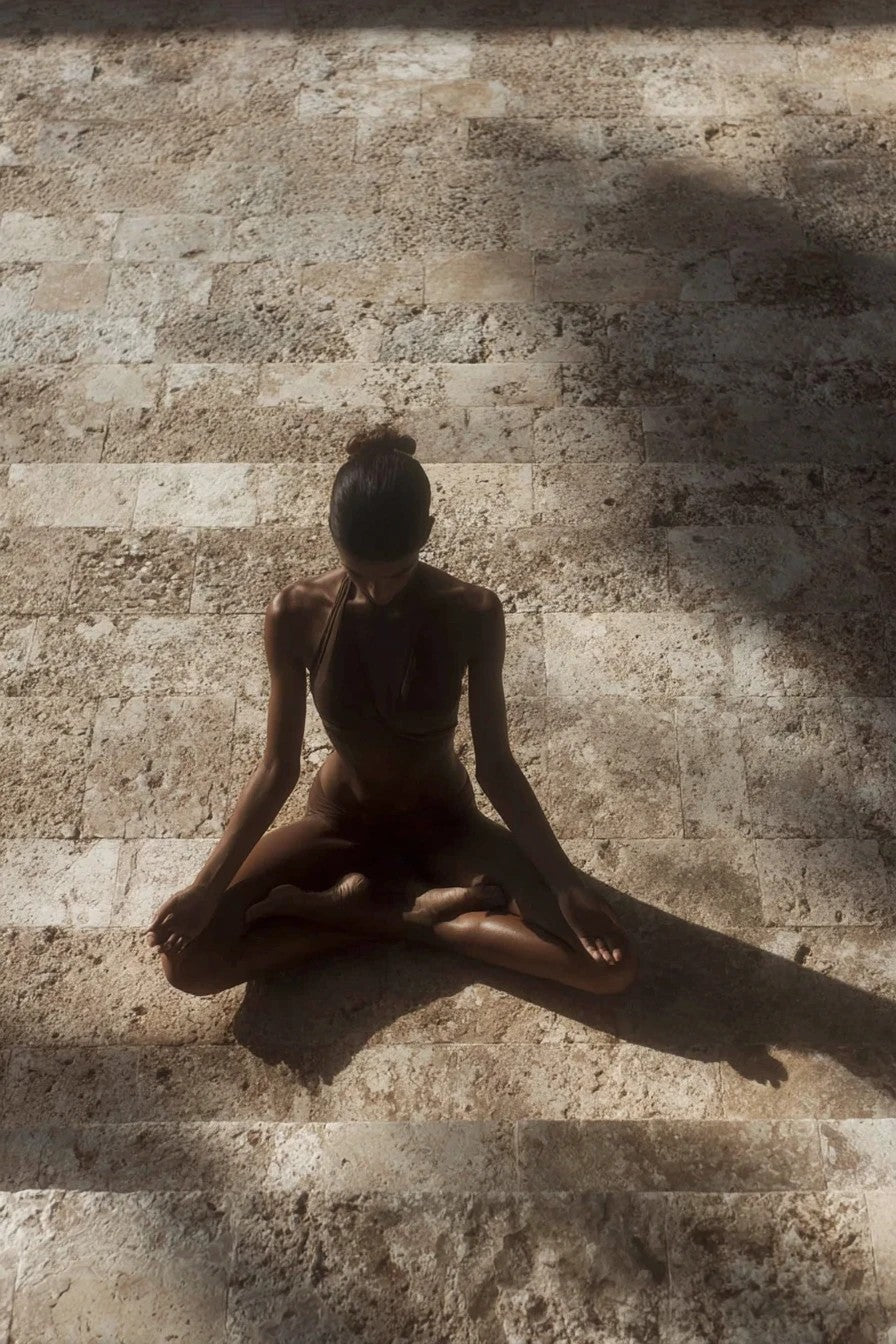 A woman seated cross-legged on sunlit travertine