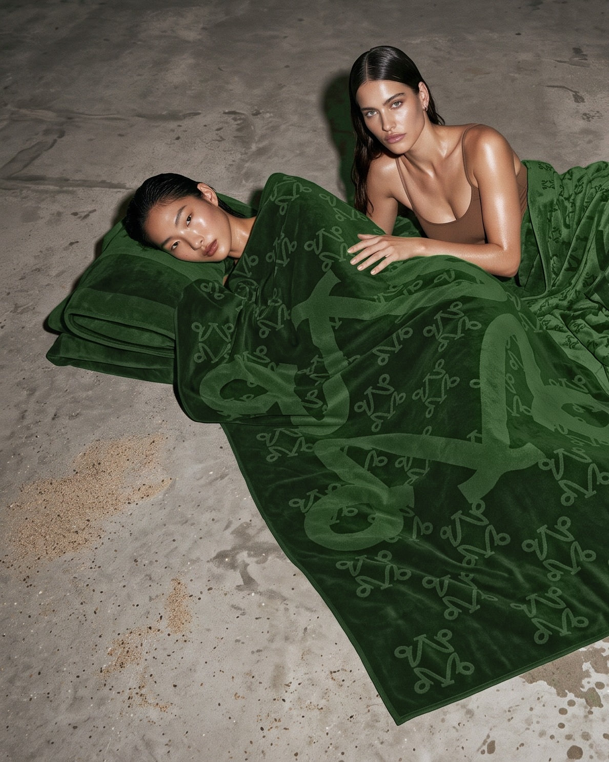 Two women resting on VELVET Undergrowth Monogram towels on a concrete floor