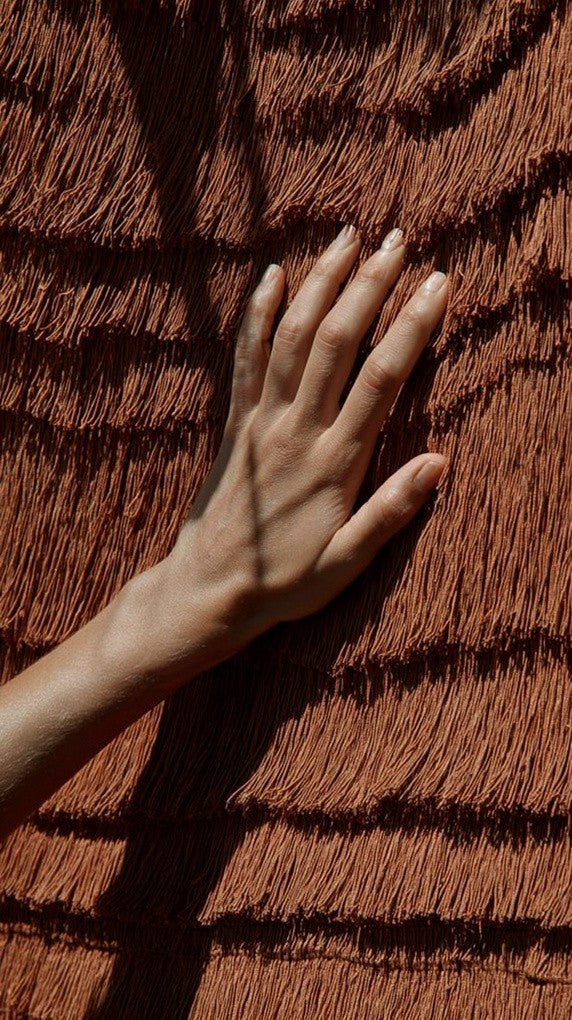 Hand resting on a terracotta-coloured towel in striped light