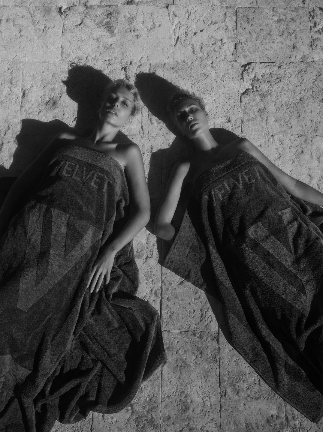 Two figures lying wrapped in VELVET monogram towels, black and white